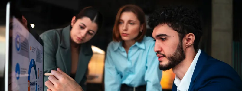 Man showing information of a computer monitor to two female colleagues